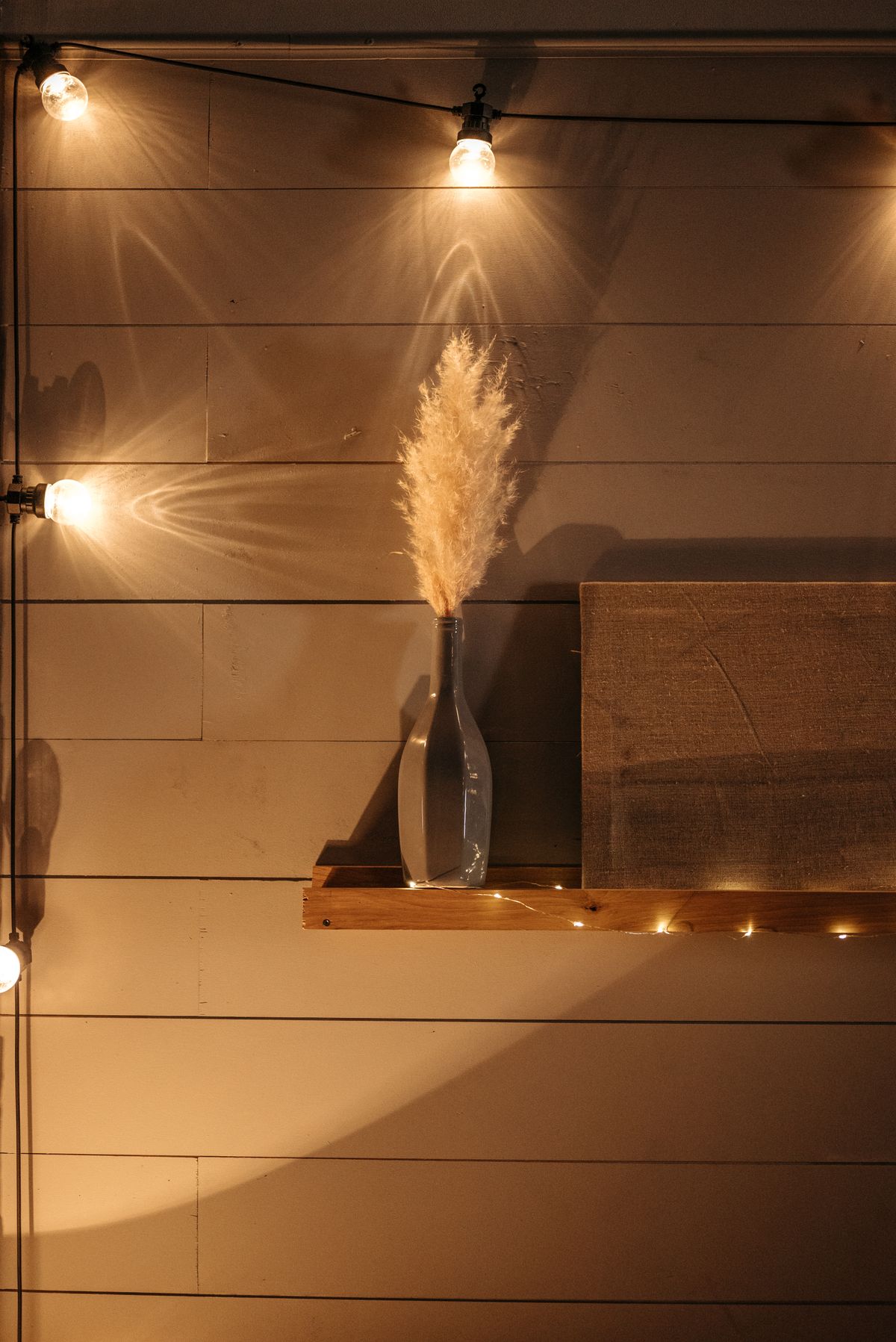 Pampas grass in a glass jar on a wooden shelf with warm light