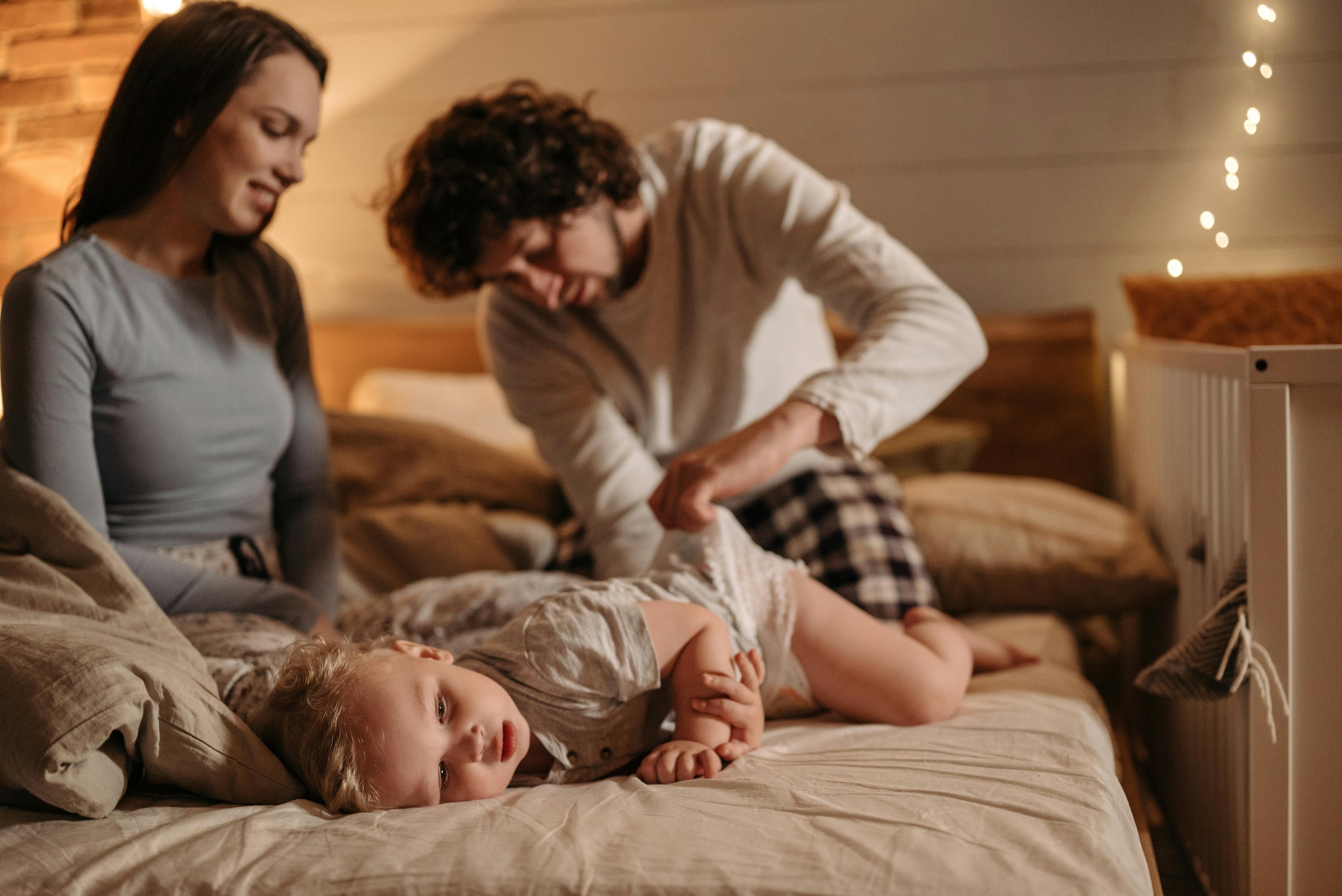 Parents enjoy bonding time with their baby while changing diaper in cozy bedroom setting.