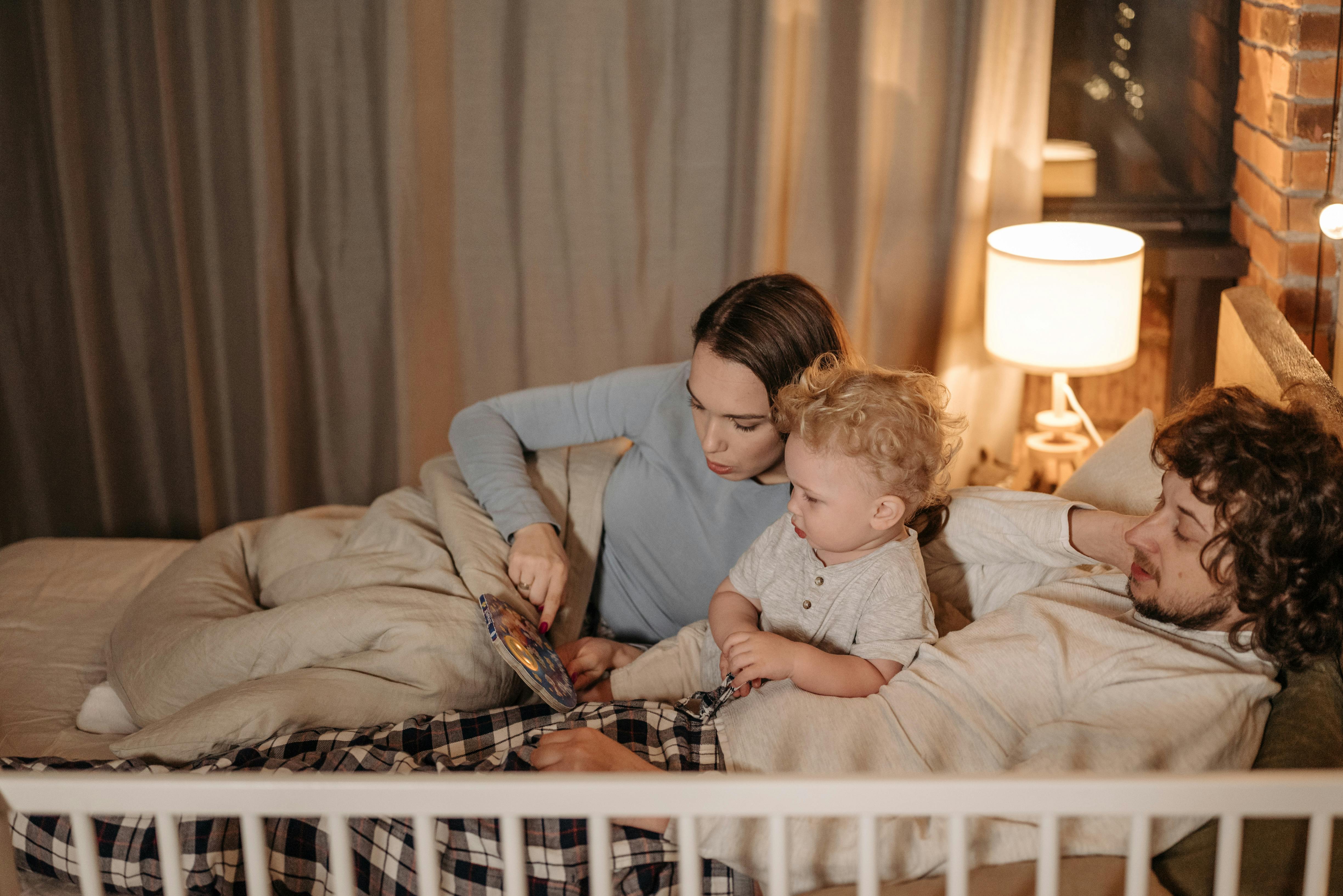 parents reading book for little boy in bed