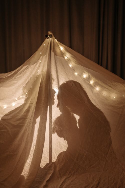 Free A silhouette of a family enjoying bonding time in a cozy blanket tent lit with string lights. Stock Photo