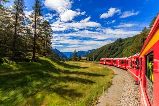 Stunning summer train ride through lush green mountains under a vibrant blue sky.