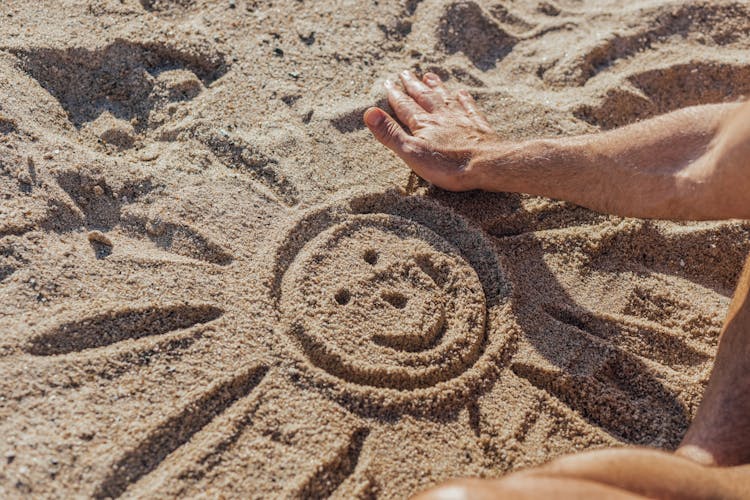 Person Drawing Smiling Sun On Sand