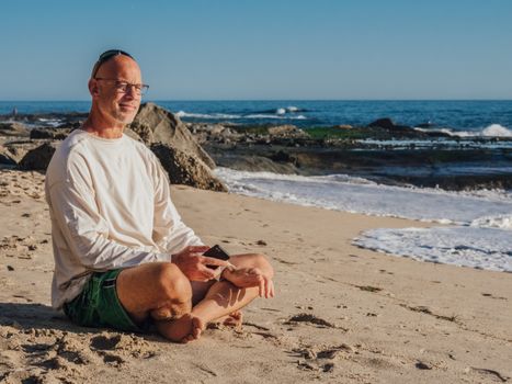 Elderly man enjoying a sunny day by the ocean on a sandy beach.