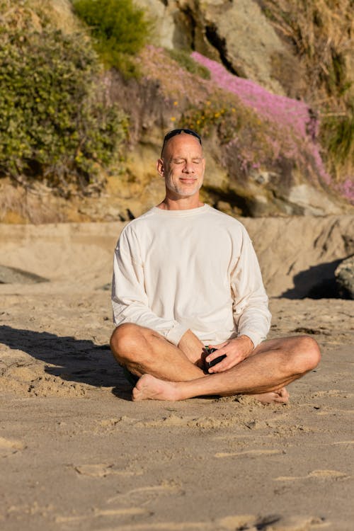 Free Bald Man Smiling and Sitting in Lotus Pose on the Beach Stock Photo