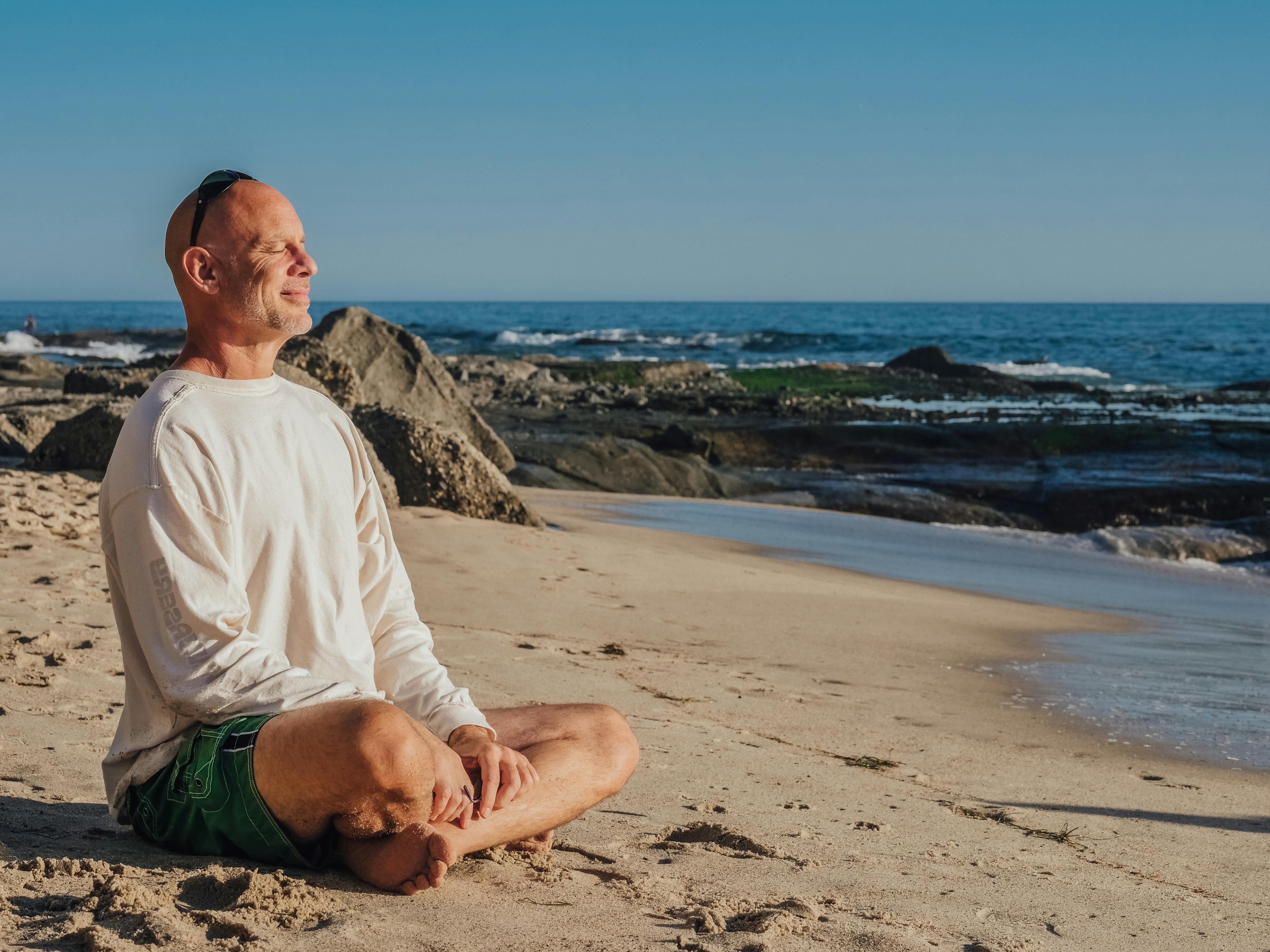 Free Bald Man Smiling While Sitting in Lotus Pose on the Beach Stock Photo