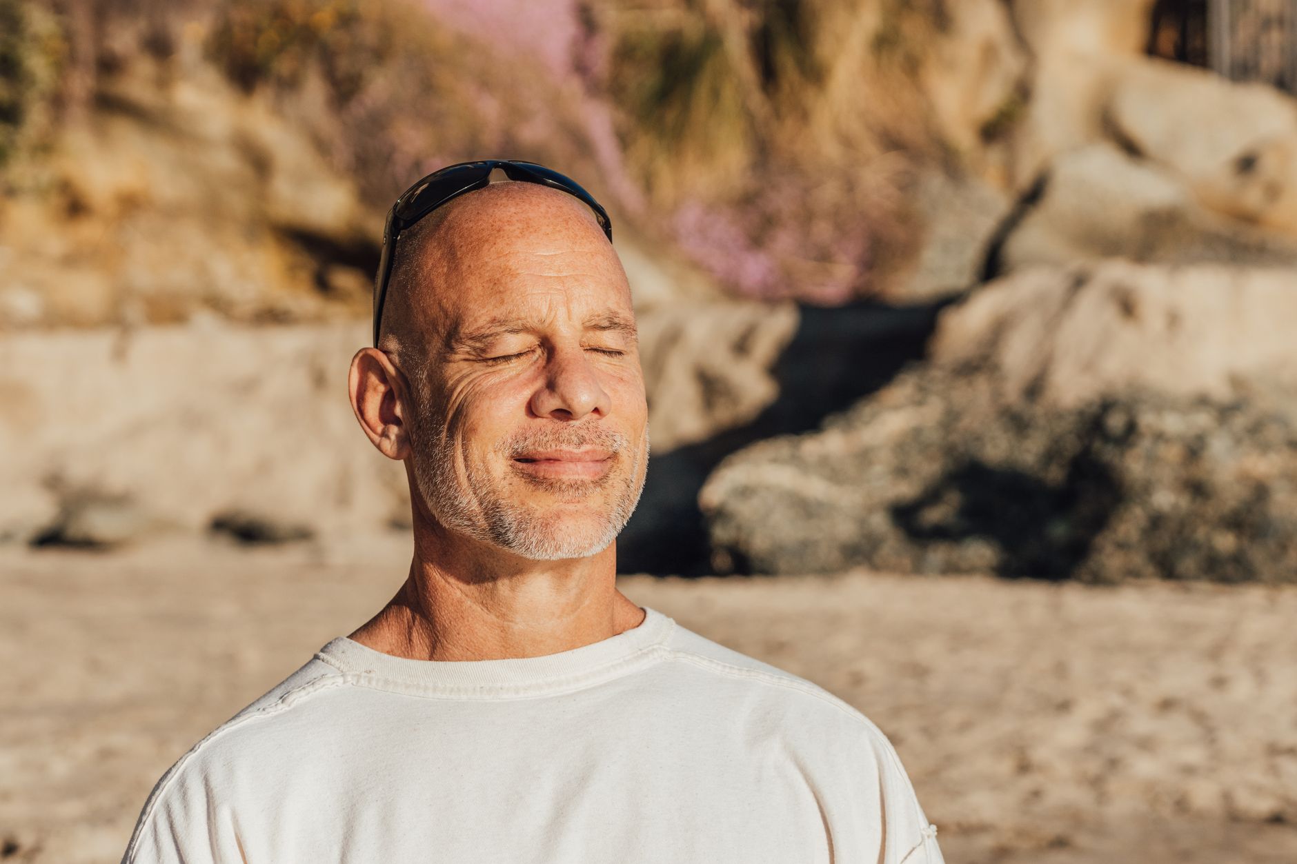 Content senior man with eyes closed, meditating and relaxing on a sunny beach day.