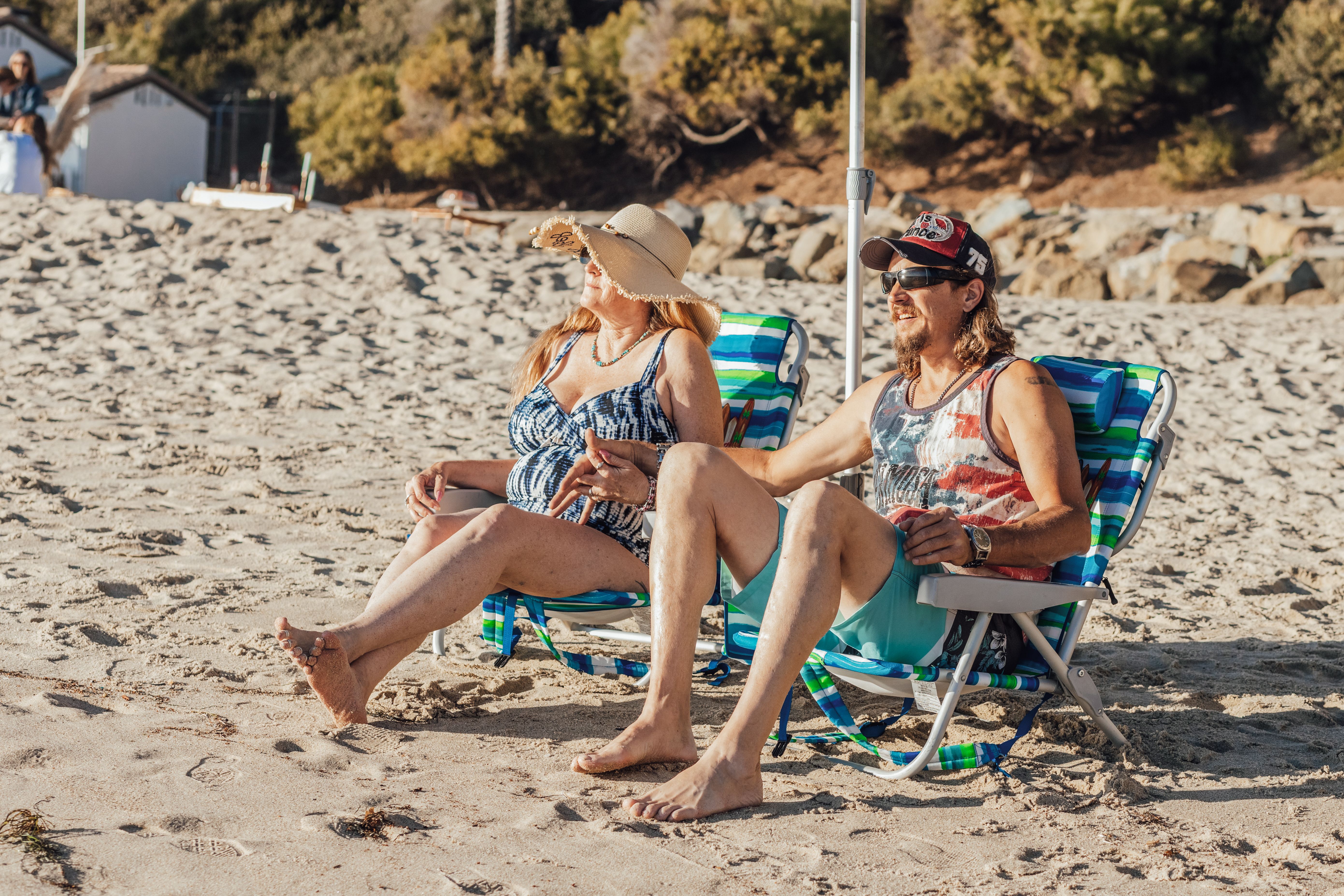 Free Elderly couple enjoying a sunny day at the beach, sitting on colorful loungers. Stock Photo