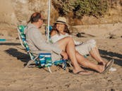 快乐的老年夫妇坐在阳光明媚的海滩上放松身心，享受假期时光