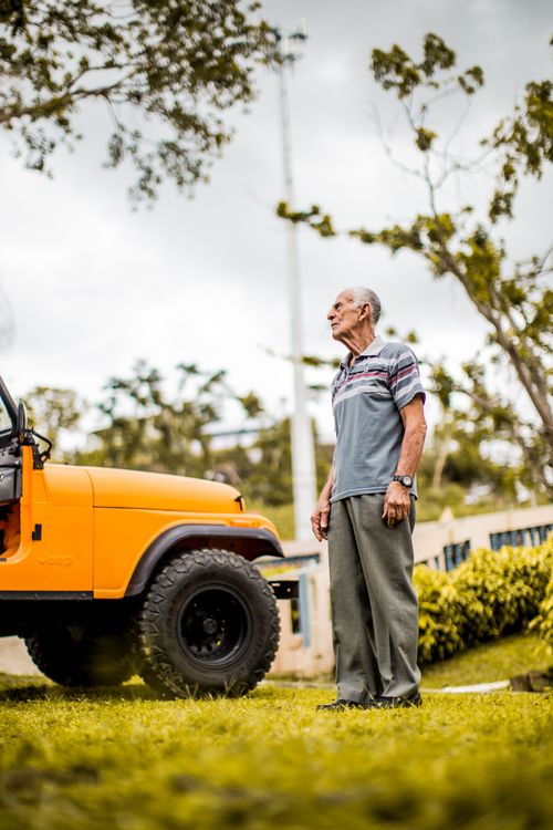 Free Elderly man standing on grass beside orange Jeep outdoors, showcasing a serene summer moment. Stock Photo