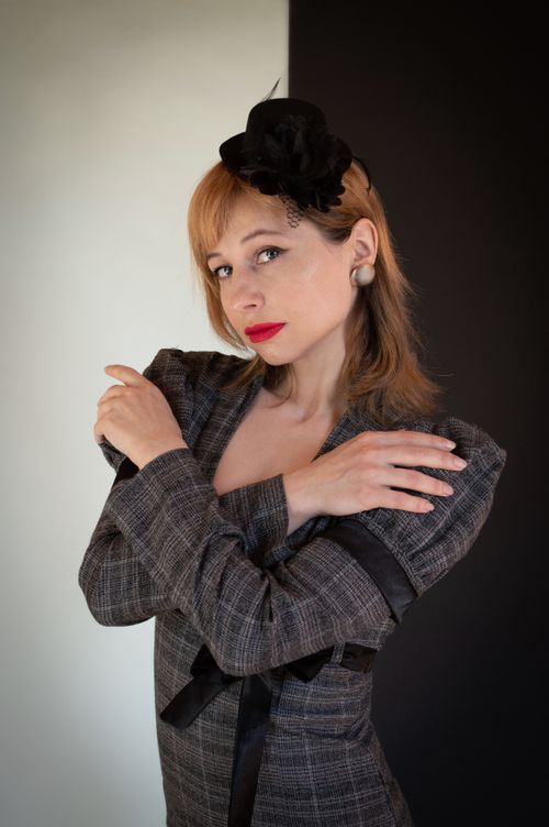 Free Elegant portrait of a woman in a stylish grey suit with a vintage hat, standing with arms crossed. Stock Photo