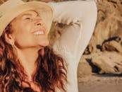 一位戴着帽子的快乐女子在海边沐浴阳光，象征着放松和幸福