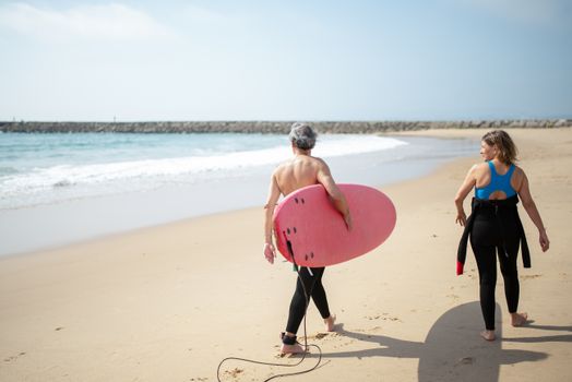 Two surfers walking along a sandy beach in Portugal, holding surfboards, ready for action.