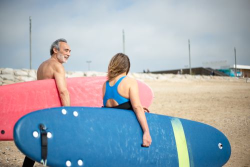 Free Man and woman carrying surfboards on a sunny beach in Portugal, ready to surf. Stock Photo