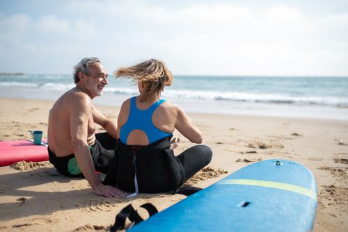 Free A man and woman enjoying a sunny day on a sandy beach in Portugal with surfboards nearby. Stock Photo