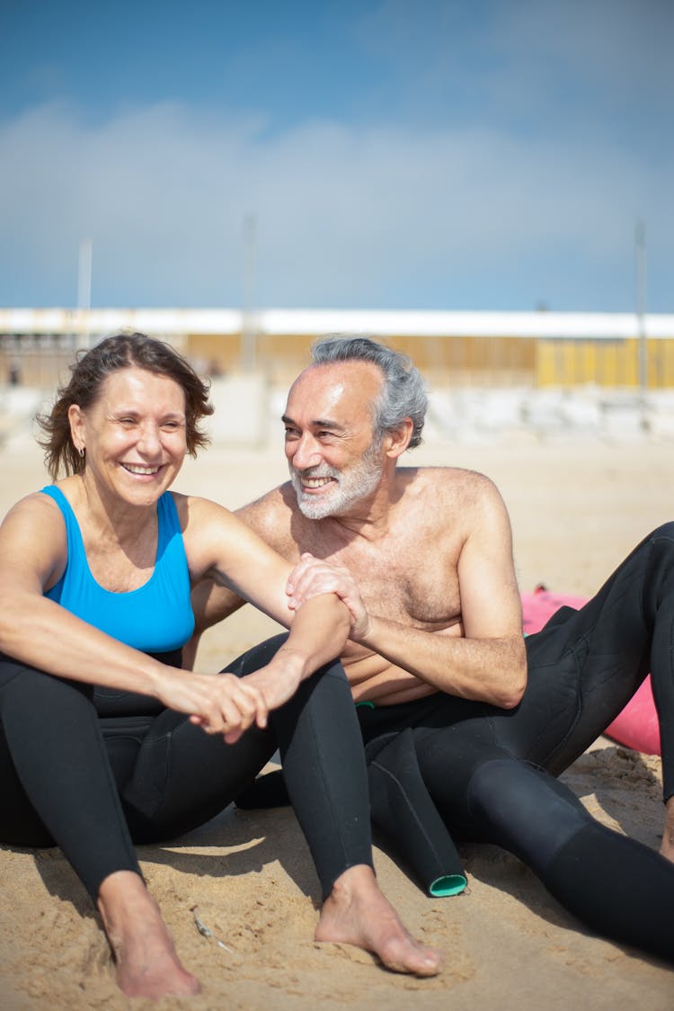 An Elderly Couple Smiling While Sitting On The Beach