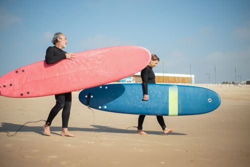Free Elderly couple carries surfboards on a sunny Portuguese beach, enjoying an active lifestyle. Stock Photo