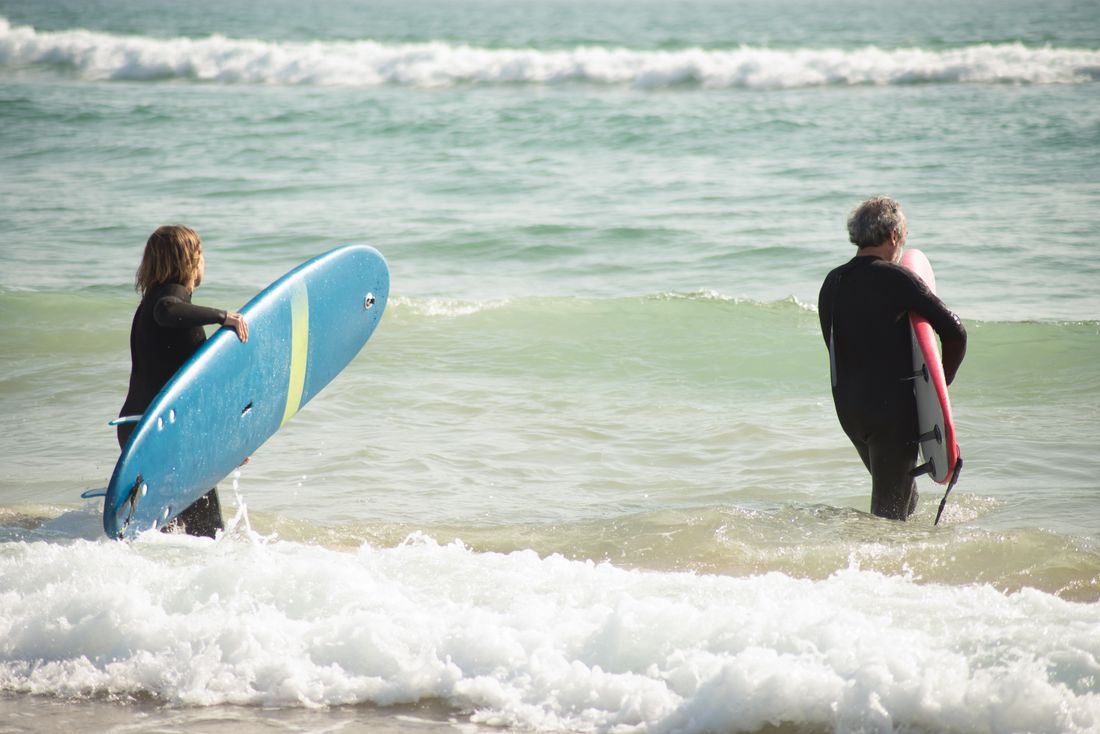 Two people walking into the ocean carrying a surfboard