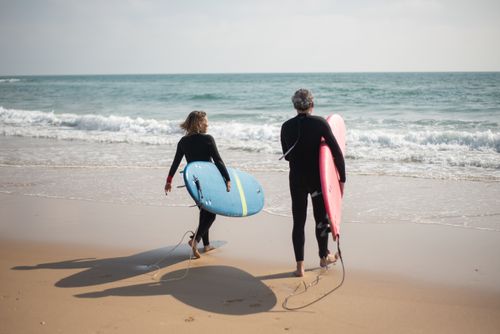 Free Seniors in wetsuits carrying surfboards on a sunny beach in Portugal. Stock Photo