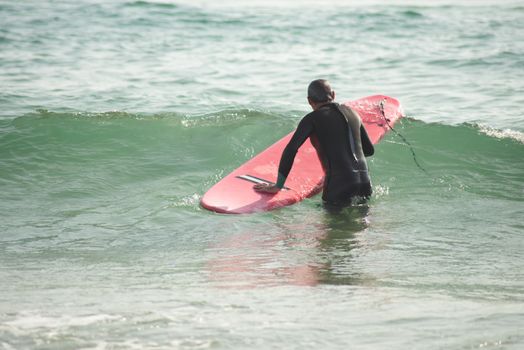 Man in Black Wetsuit Holding Red Surfboard on Water
