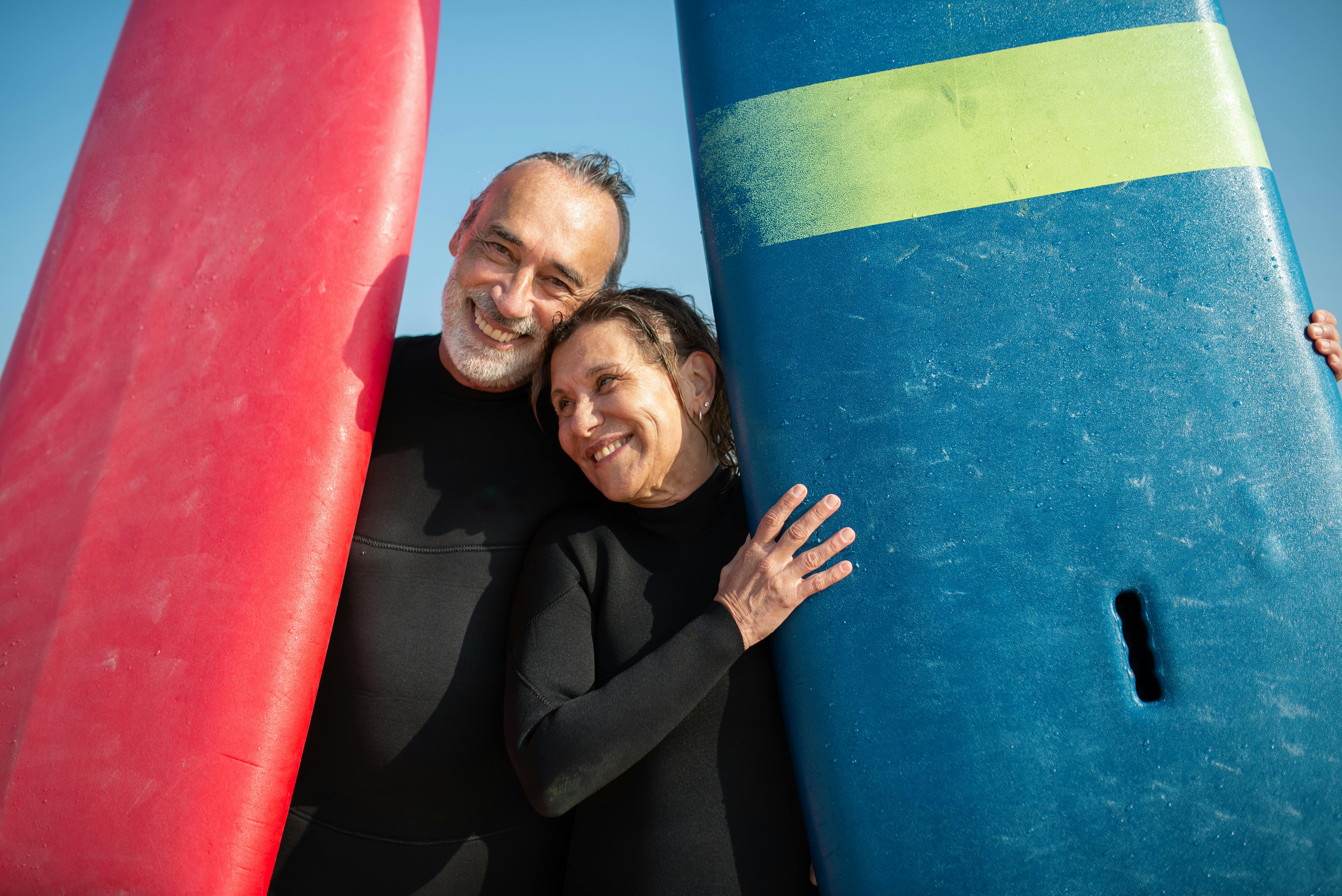 微笑的夫妇拿着冲浪板在一个阳光明媚的海滩，享受休闲时间.