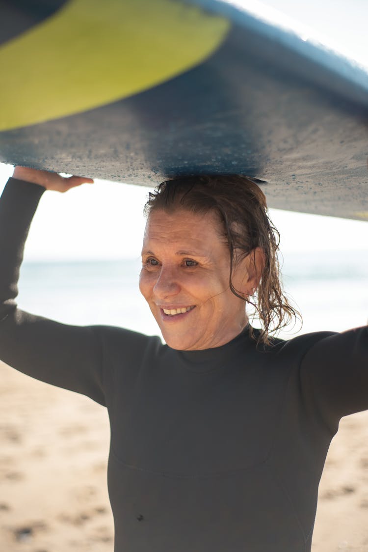 An Elderly Woman Carrying A Surfboard 