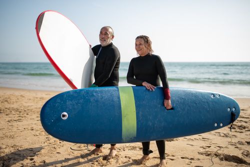 Free Senior couple enjoying a sunny beach day in Portugal with surfboards. Stock Photo