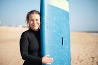 在葡萄牙阳光明媚的海滩上，年长的女性手持冲浪板微笑，准备好冲浪冒险