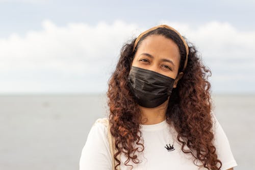 A Woman with Curly Hair Wearing Black Face Mask while Looking at the Camera