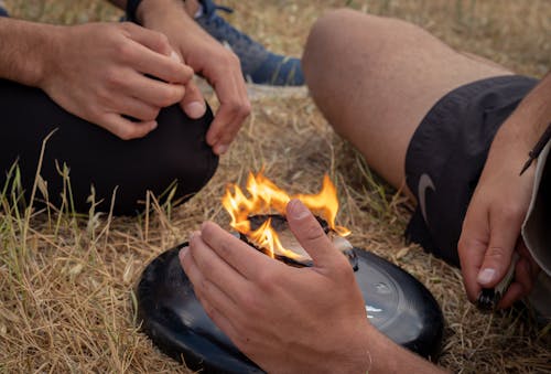 Free From above of crop anonymous men friends sitting near burning camping stove in nature in daytime Stock Photo