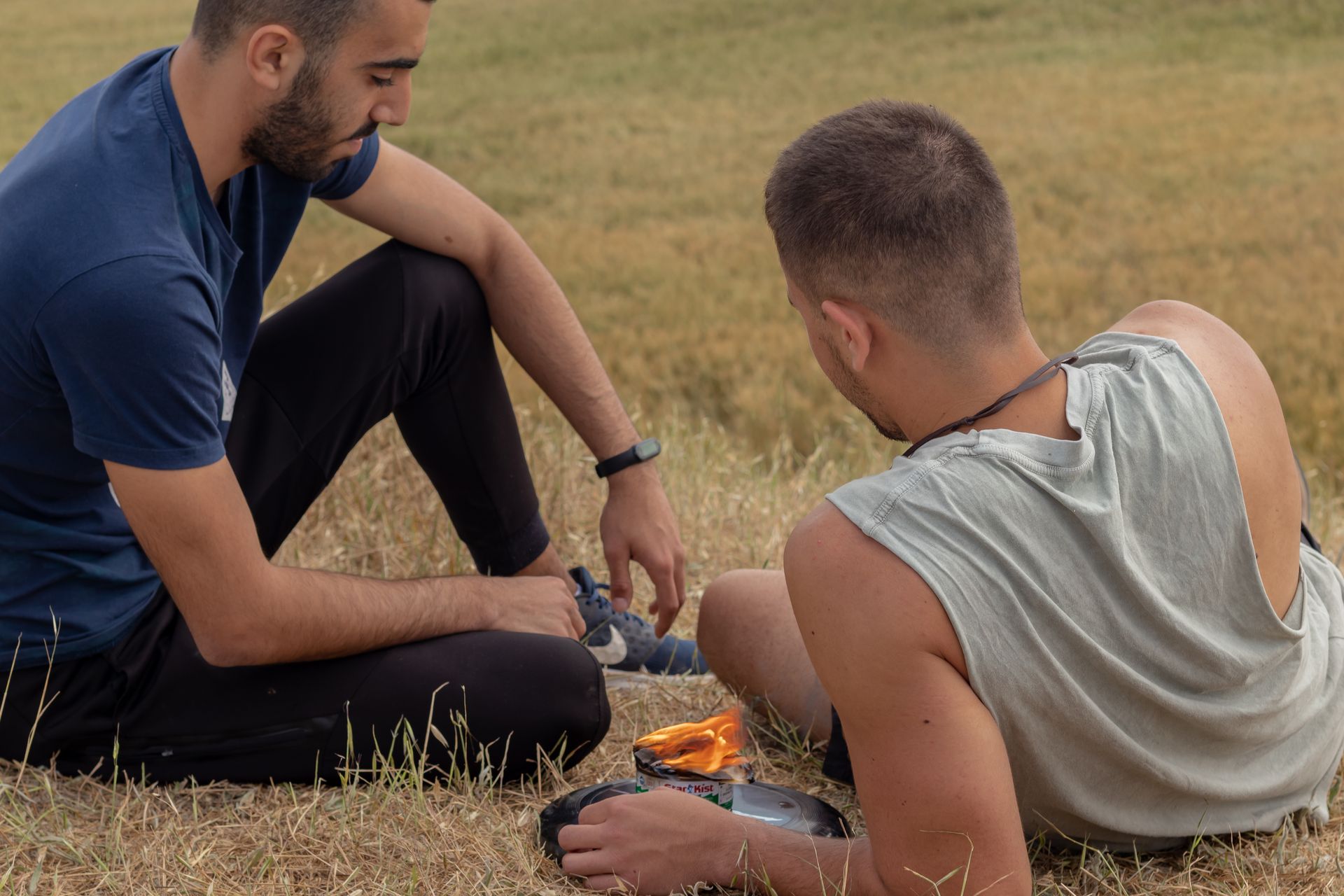 Two men sitting outdoors in a grassy field with a portable fire during a relaxing summer picnic.