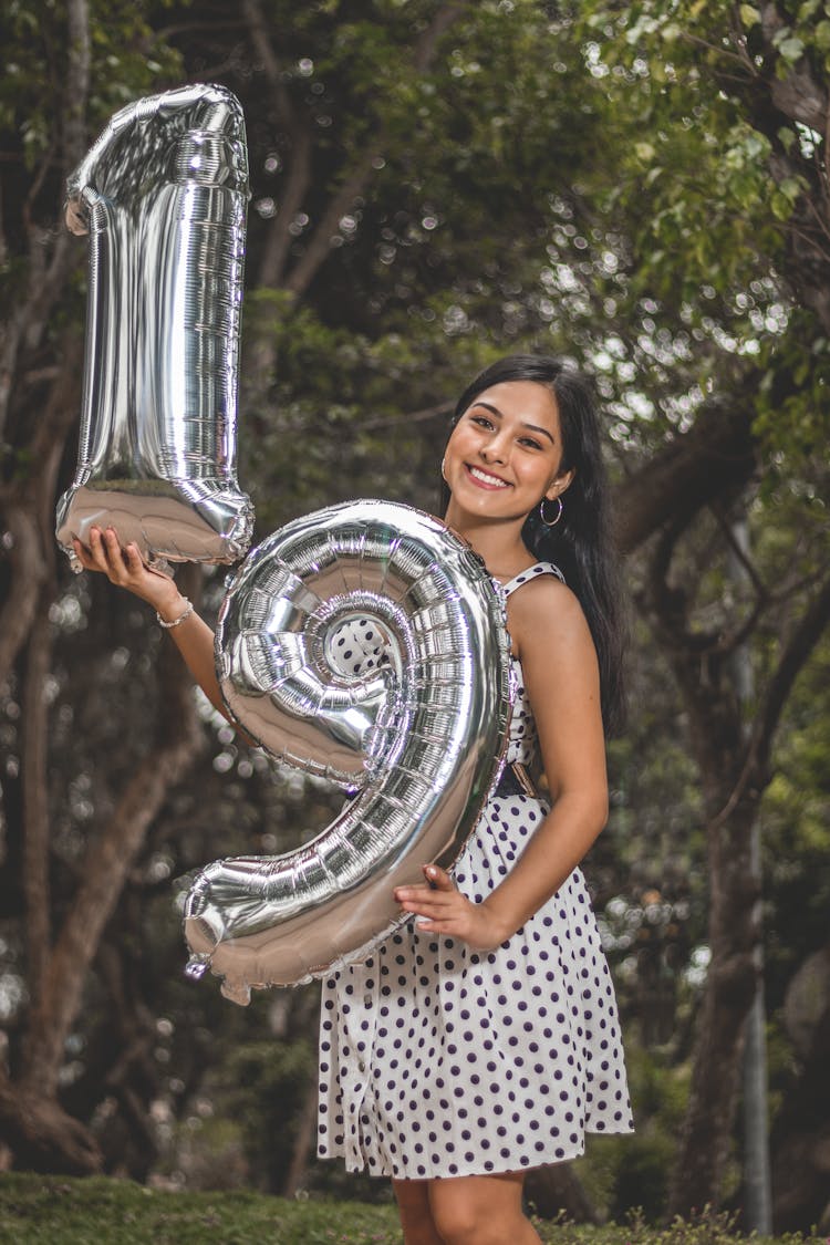 A Woman Smiling At The Camera While Holding Number Balloons