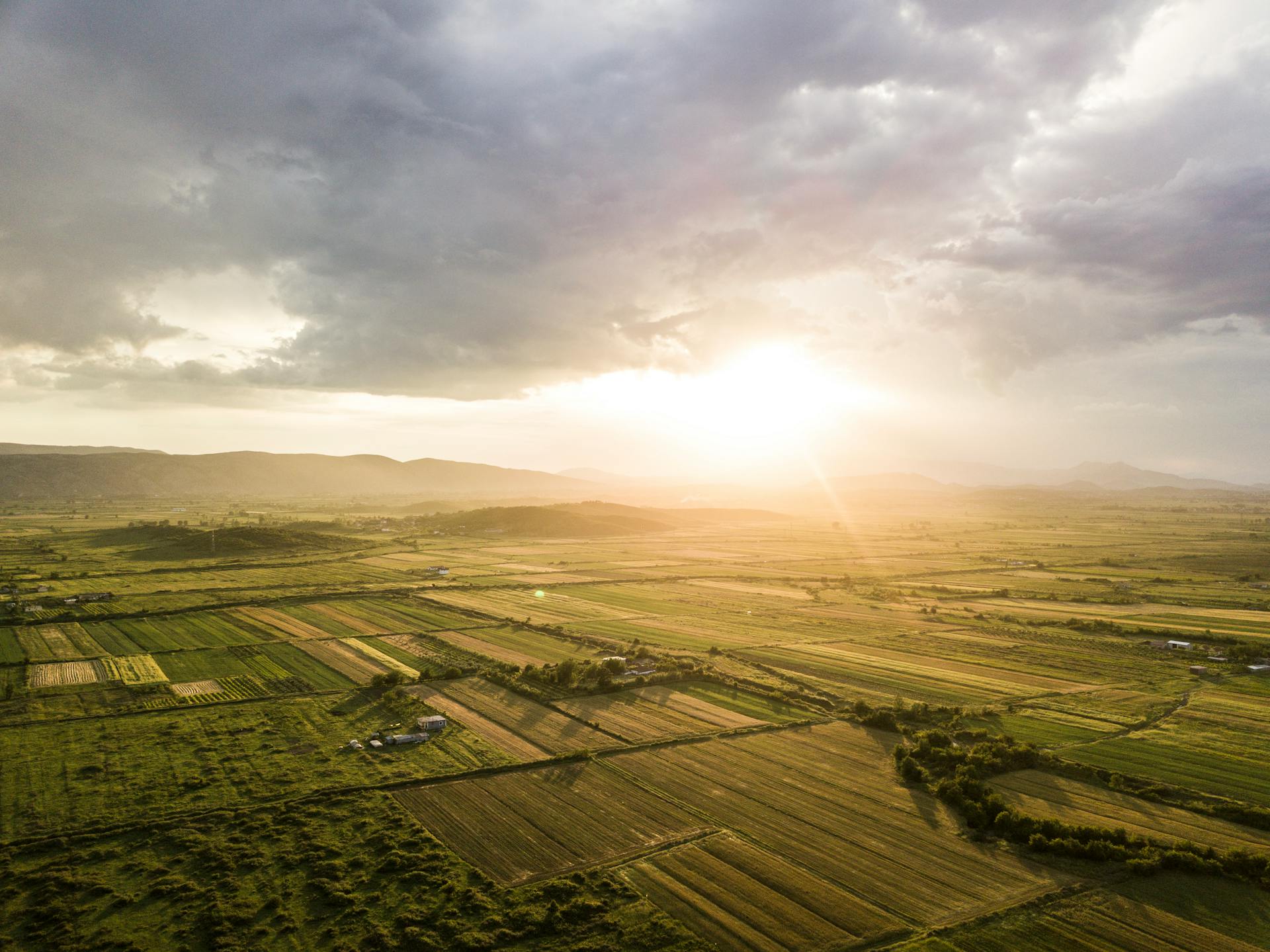 Stunning aerial shot of Albanian farmland with dramatic clouds and sunset lighting.