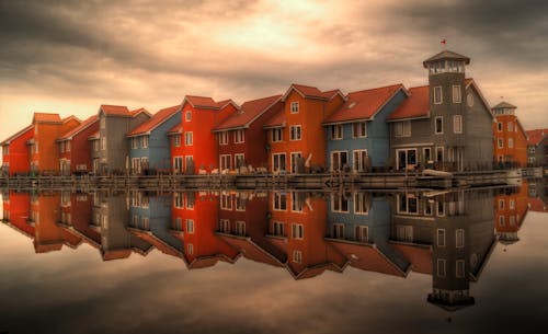 Assorted-color House Near Water Mirror Reflector Under Cloudy Sky during Golden Hour