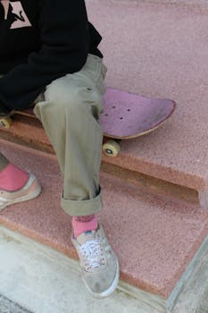 Person in casual attire sitting with a skateboard on outdoor steps.