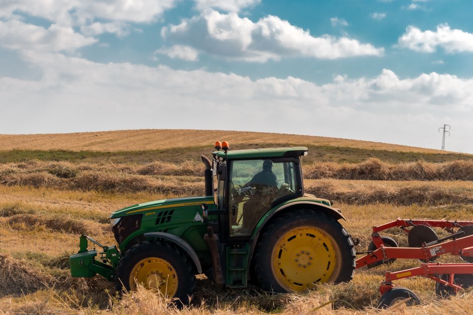 Un tractor verde arando un campo dorado bajo un cielo azul con nubes dispersas.