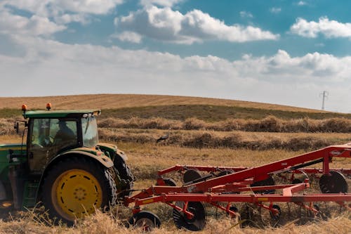 Unrecognizable farmer in tractor ploughing grassy field