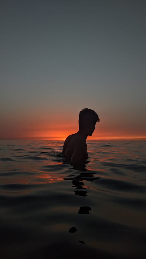 Free Silhouette of a Man in a Body of Water at Sunset Stock Photo