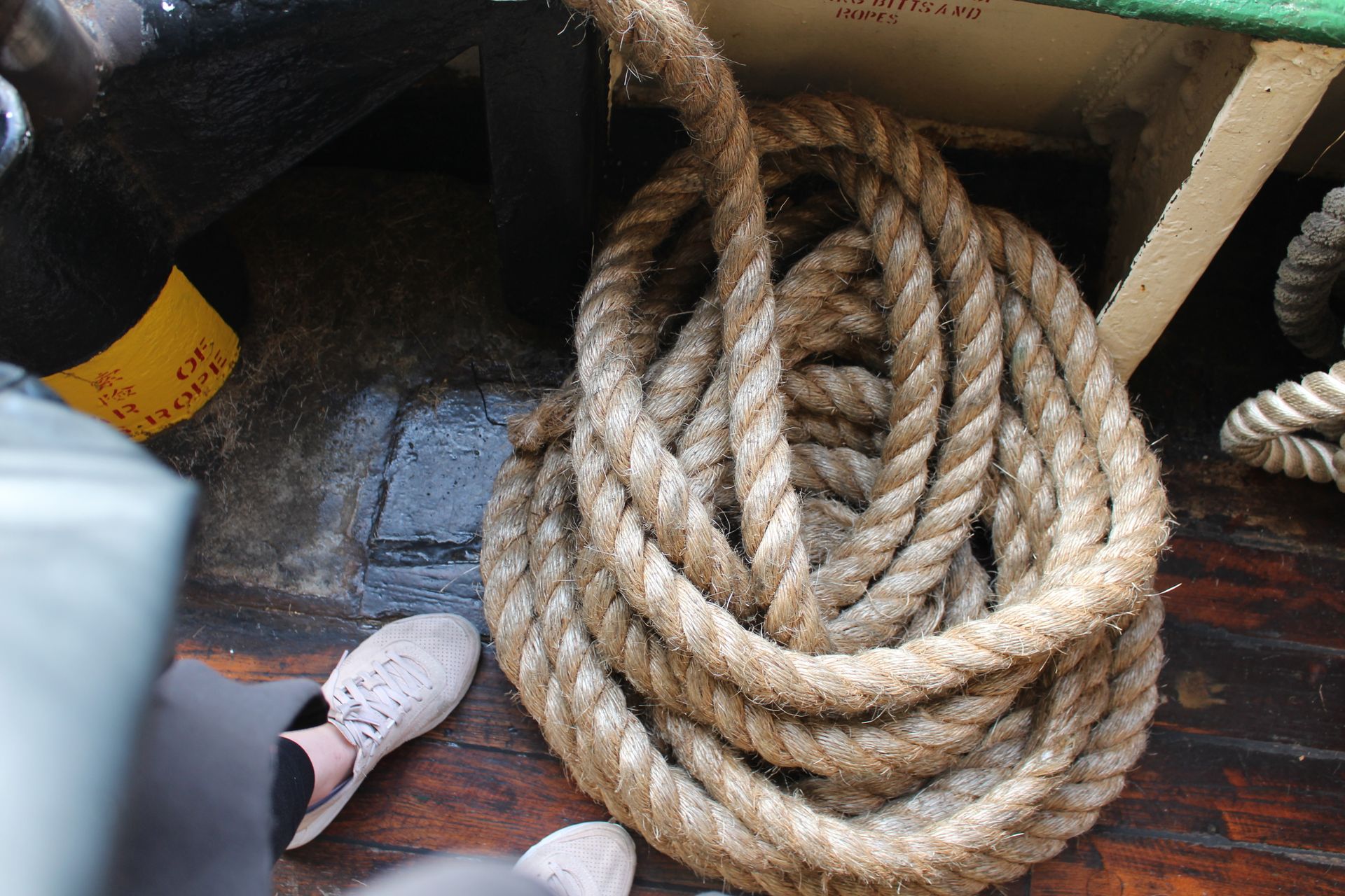 Close-up of a coiled rope on a wooden ship deck with partial shoes visible.