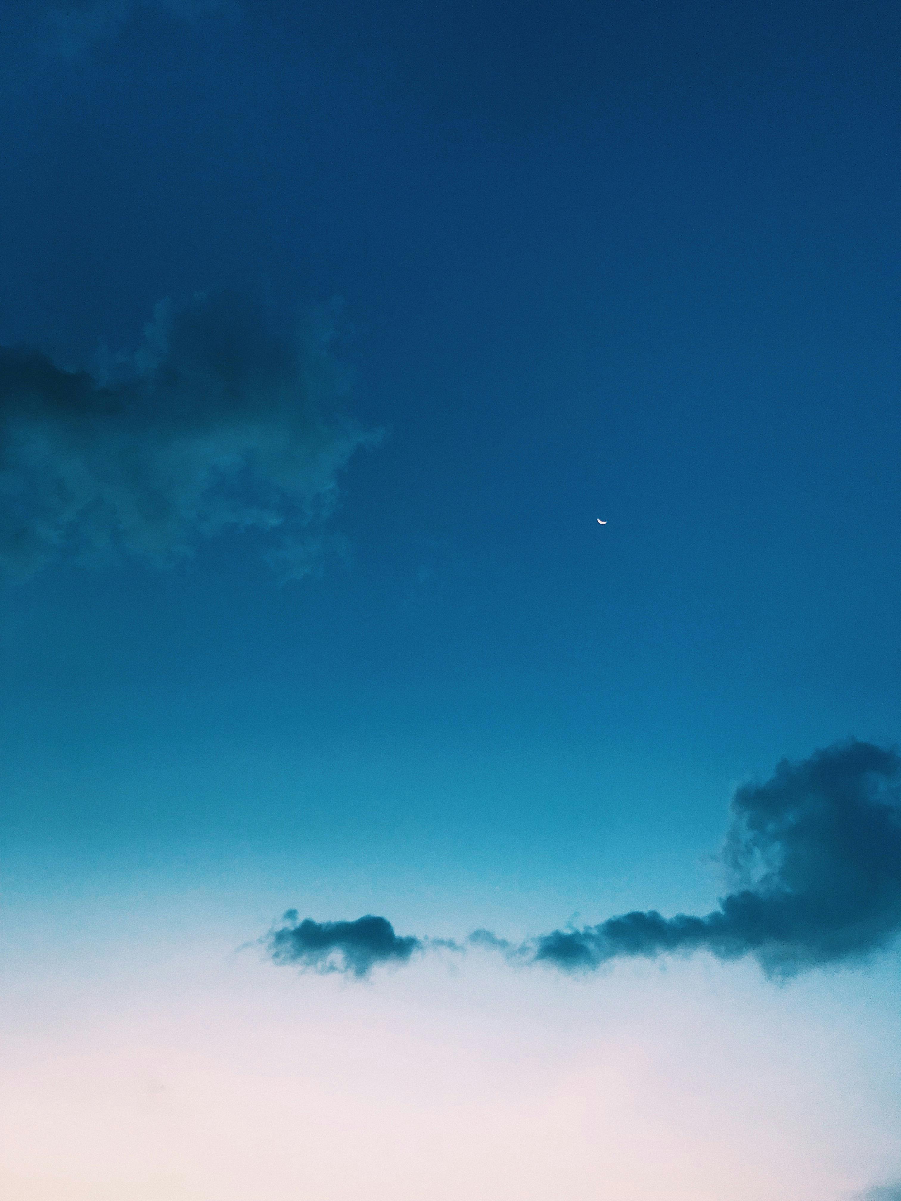 A tranquil evening sky over Bali featuring a crescent moon and soft clouds.