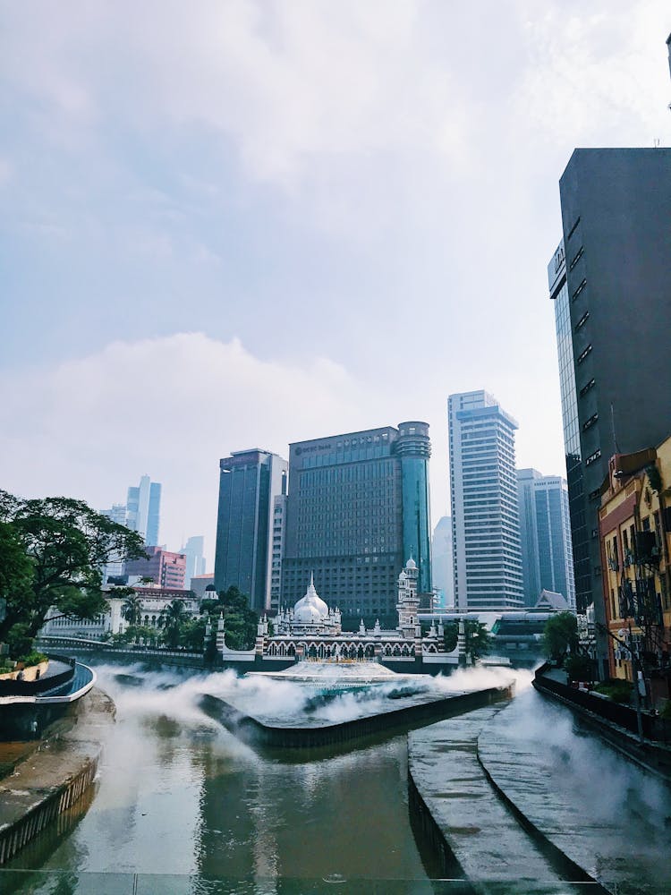 Pond Near City Buildings Under White Cloudy Sky