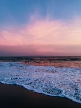 A tranquil scene of a Bali beach at sunset with pink and blue hues over the ocean.