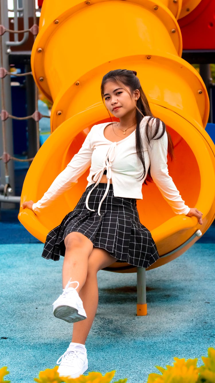 A Woman Sitting On The Edge Of A Yellow Slide At The Park