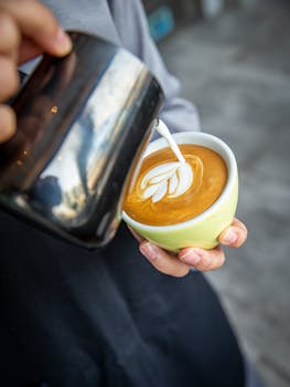 Barista skillfully pouring milk to create beautiful latte art in a vibrant cup.