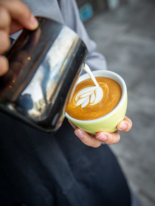 Free Barista skillfully pouring milk to create beautiful latte art in a vibrant cup. Stock Photo