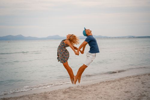 Free A joyful couple jumps on the beach, forming a heart shape, capturing love and travel spirit. Stock Photo