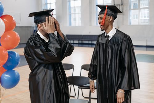 Free Two graduates sharing a joyful moment in caps and gowns indoors. Stock Photo