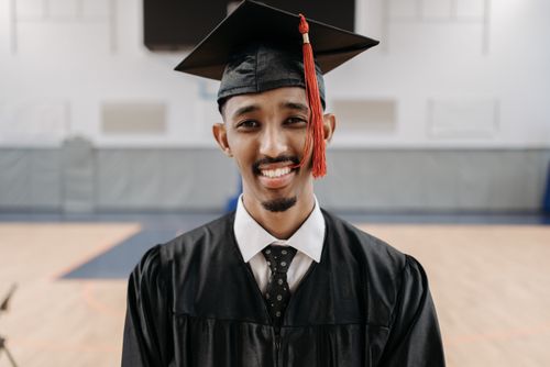 Free Young man celebrating graduation with a smile, wearing cap and gown indoors. Stock Photo