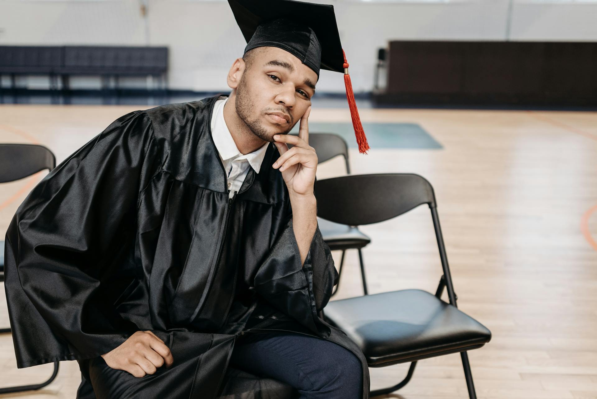 Confident college graduate sitting in ceremony with cap and gown.