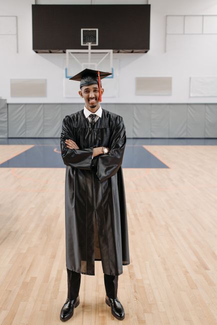 A happy graduate in cap and gown stands confidently in a gymnasium. A happy graduate in cap and gown stands confidently in a gymnasium.