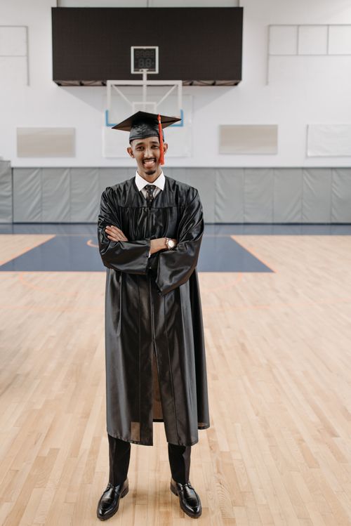 Free A happy graduate in cap and gown stands confidently in a gymnasium. Stock Photo